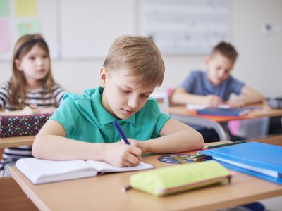 Schoolboy writing in exercise book in class
